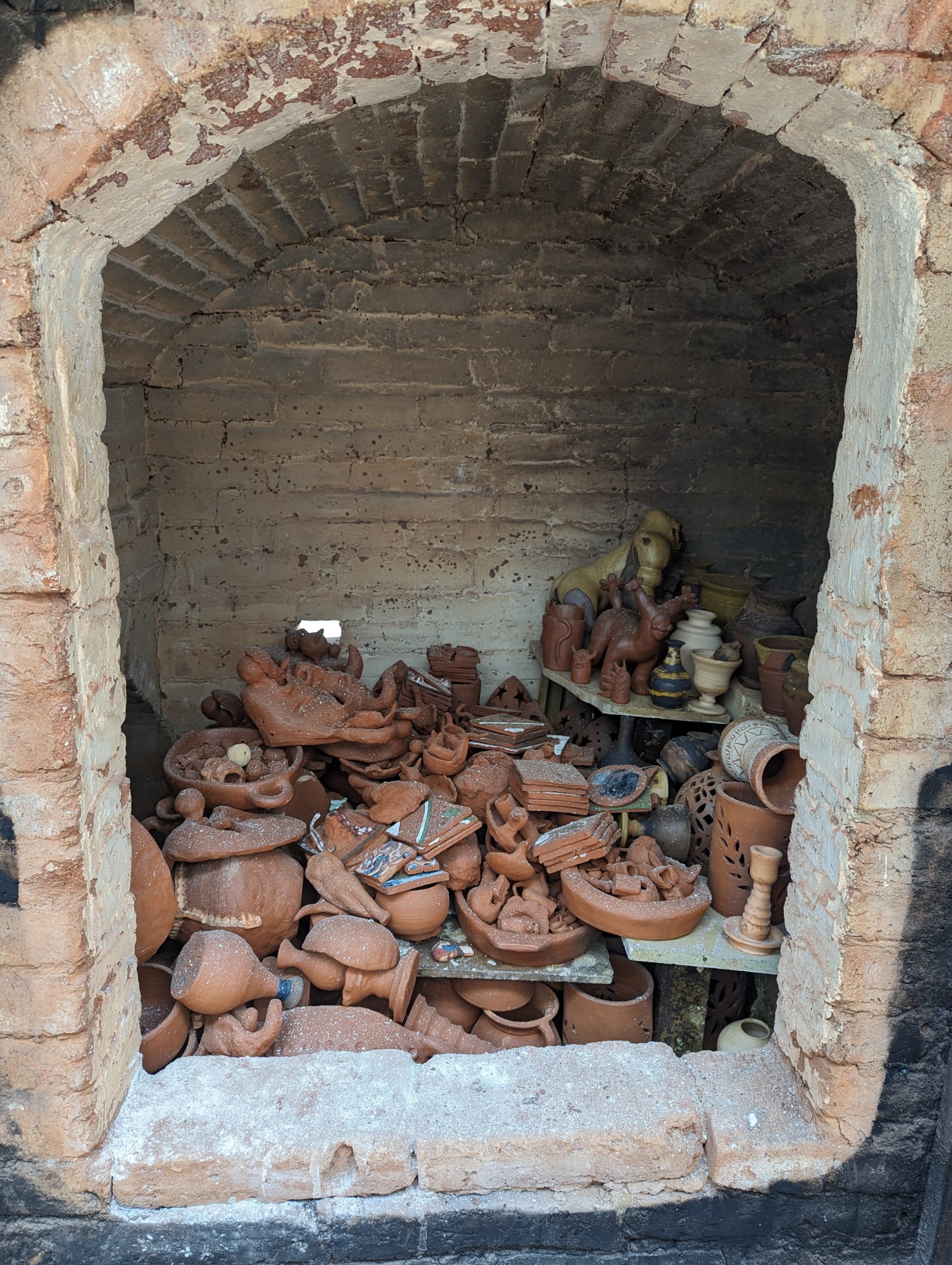 Looking through the open door of a brick kiln, we see ceramic vases, bowls, and dishes piled on top of each other with a thin layer of ash coating everything.